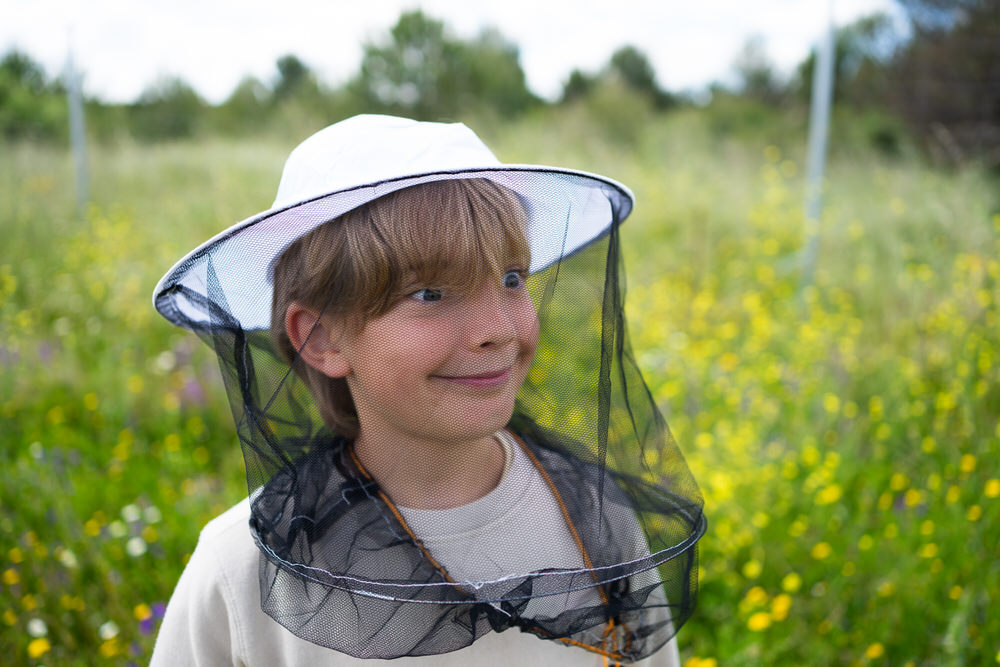 Boy wearing beekeeping gear standing in a vibrant wildflower field